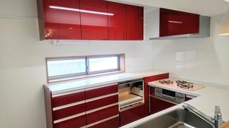 コンパクトな空間に機能的なレイアウト。ディープレッド扉がアクセントの美しく使いやすいシステムキッチン。